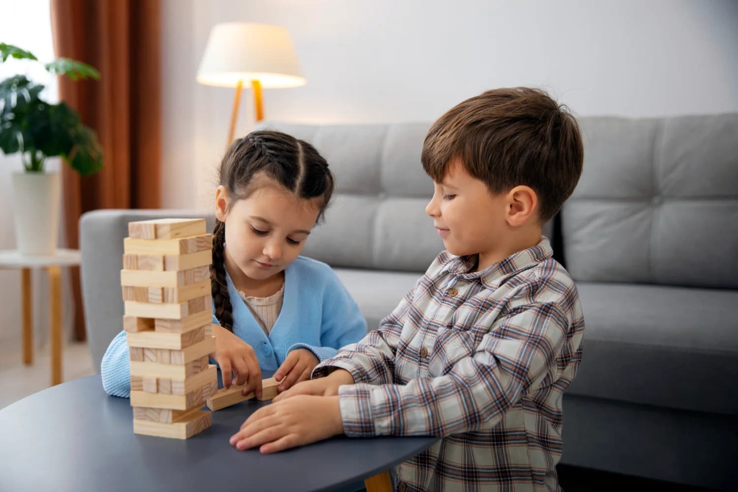 Two children playing with small wooden bricks tower togather